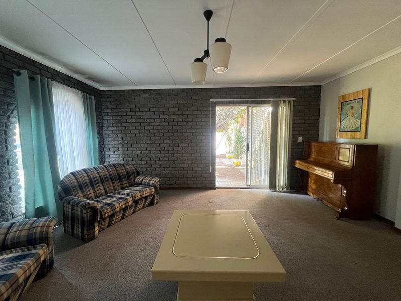 Spacious living room featuring an exposed brick feature wall, carpeted flooring, and a sliding glass door providing access to the outdoor area.