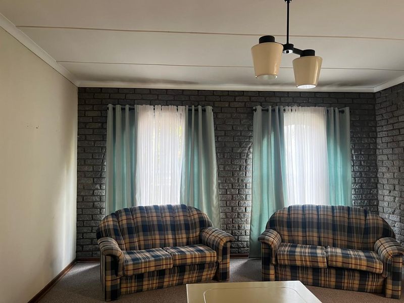 A living room featuring a textured exposed brick wall, neutral carpeting, and a classic ceiling pendant light fixture.