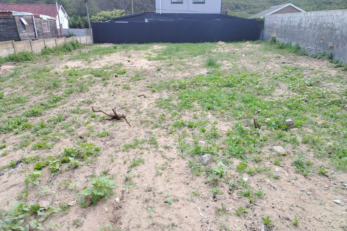 A vacant residential plot featuring sandy soil, perimeter boundary walls, and corrugated metal fencing, ready for development.