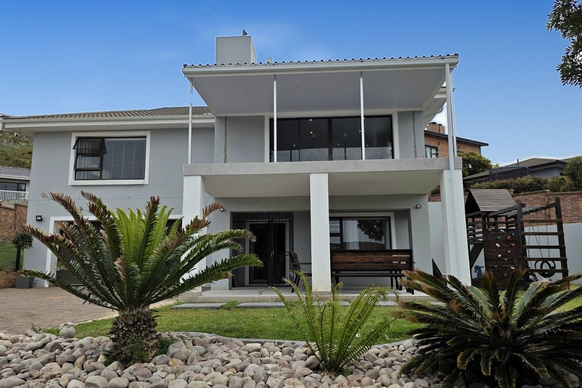 Rear view of a two-story house featuring a covered ground-floor patio, an upper-level balcony, and a landscaped garden with a paved area.