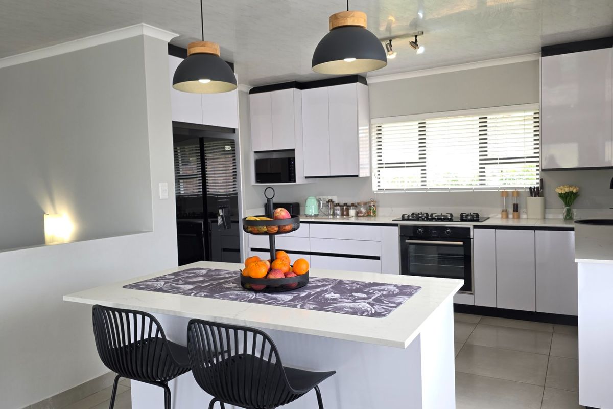 Modern kitchen featuring a central island with quartz countertops, sleek white cabinetry, built-in oven, gas hob, and contemporary pendant lighting.