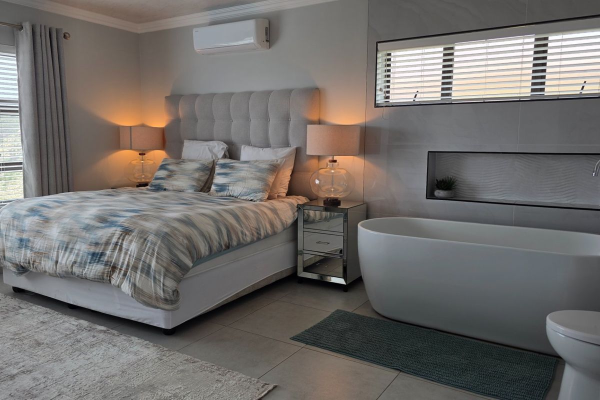 A modern, open-plan bedroom suite featuring a freestanding bathtub, tiled flooring, recessed wall niche, and integrated air conditioning for a luxurious, contemporary feel.