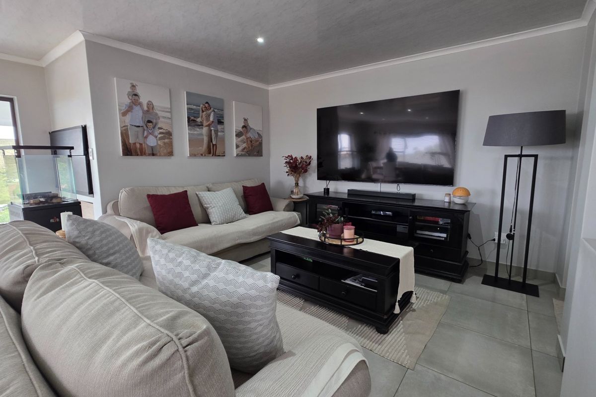 A well-maintained living room featuring neutral tiled flooring, recessed lighting, and a large sliding glass door providing natural light and outdoor access.