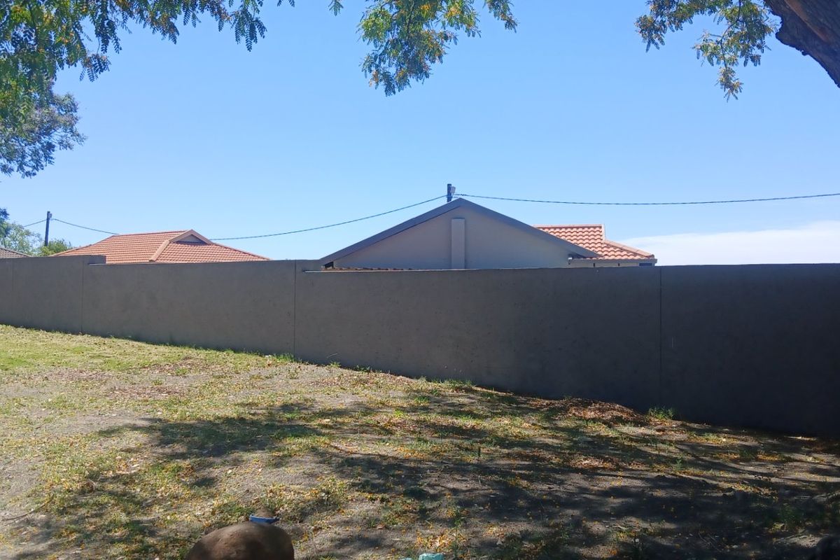 A view of the rear garden area featuring a solid perimeter boundary wall and mature trees.