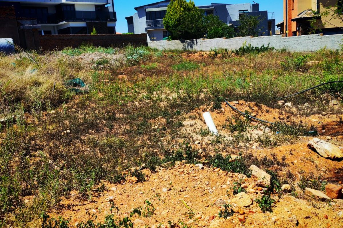 A vacant residential plot featuring uneven terrain, exposed soil, and a perimeter boundary wall, situated in a developed neighborhood.