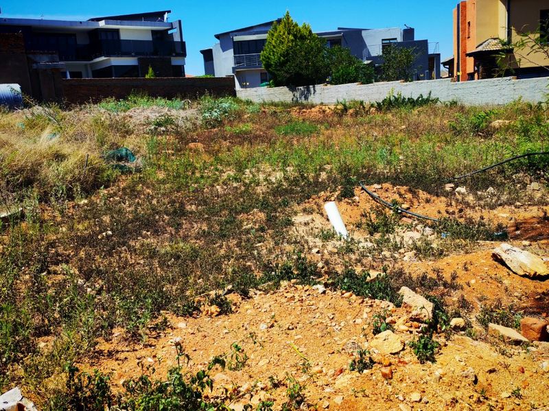 A vacant residential plot featuring uneven terrain, exposed soil, and a perimeter boundary wall, situated in a developed neighborhood.