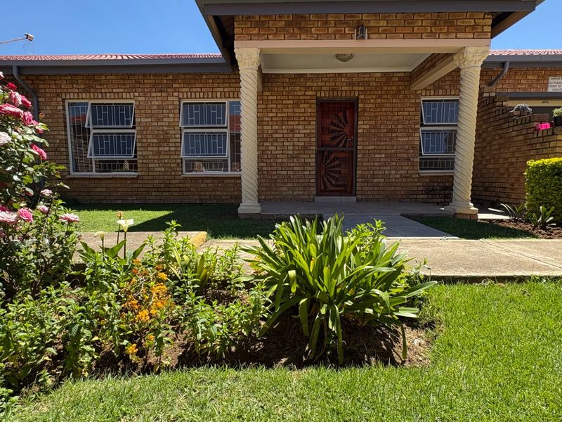 Front elevation of a face brick house featuring a covered entrance with decorative columns, security bars on windows, and a well-maintained front garden.