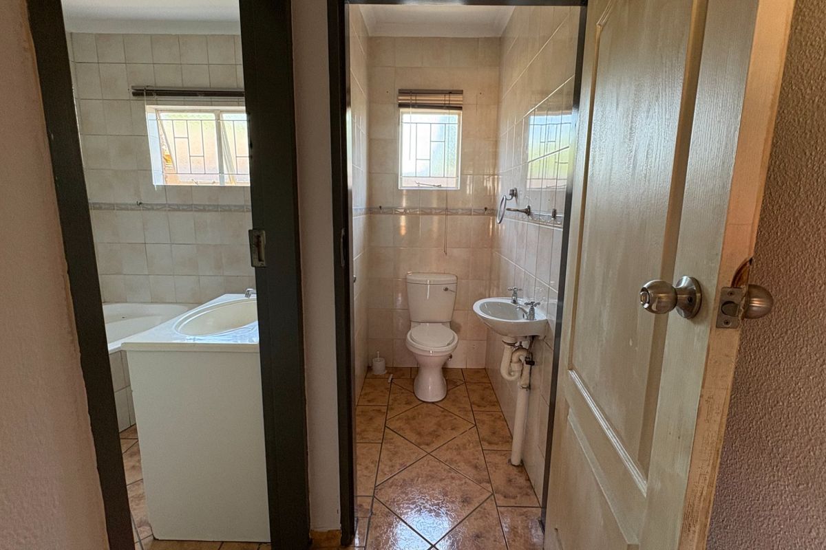 A functional bathroom featuring tiled walls and floors, a pedestal basin, and a built-in bathtub, offering a clean and practical layout.