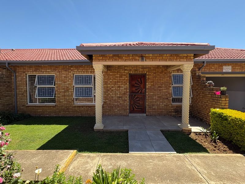 Front elevation of a face brick house featuring a covered entrance with decorative columns, security gates, and a paved walkway leading to the front door.