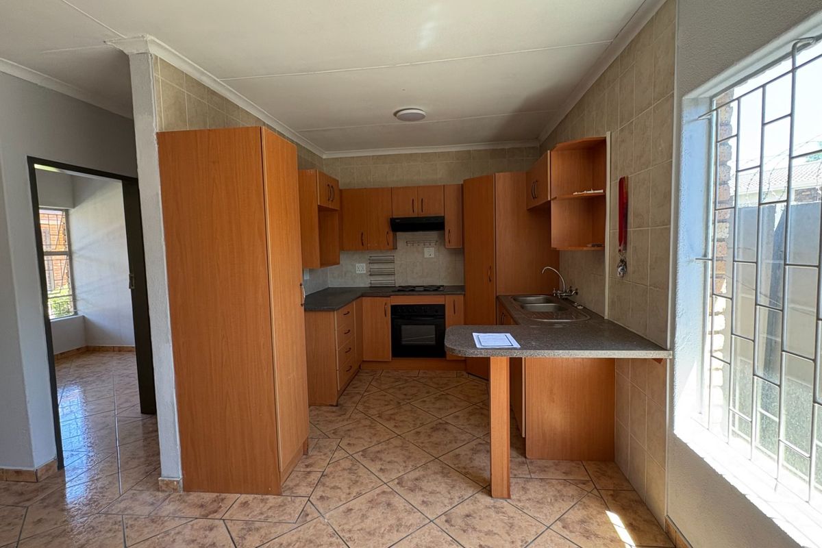 A functional kitchen featuring built-in wooden cabinetry, laminate countertops, an integrated oven with extractor fan, and tiled flooring throughout.