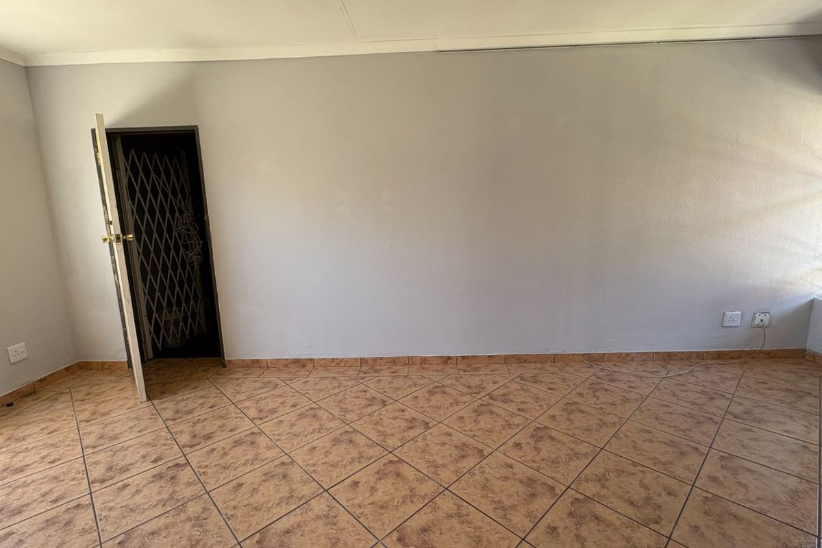 An empty bedroom featuring tiled flooring, a security gate at the entrance, and a window fitted with security bars.