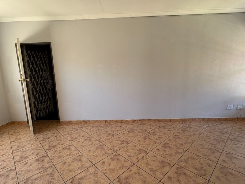 An empty bedroom featuring tiled flooring, a security gate at the entrance, and a window fitted with security bars.