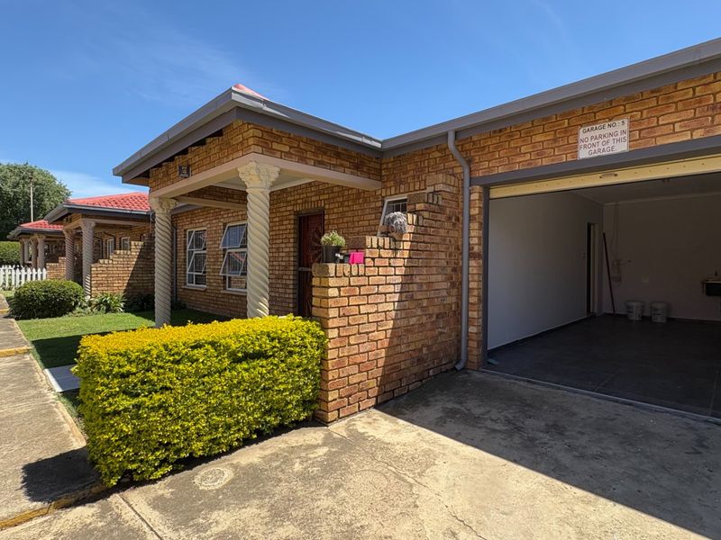 Front view of a face brick residential unit featuring a covered entrance, a single garage, and a well-maintained garden area.