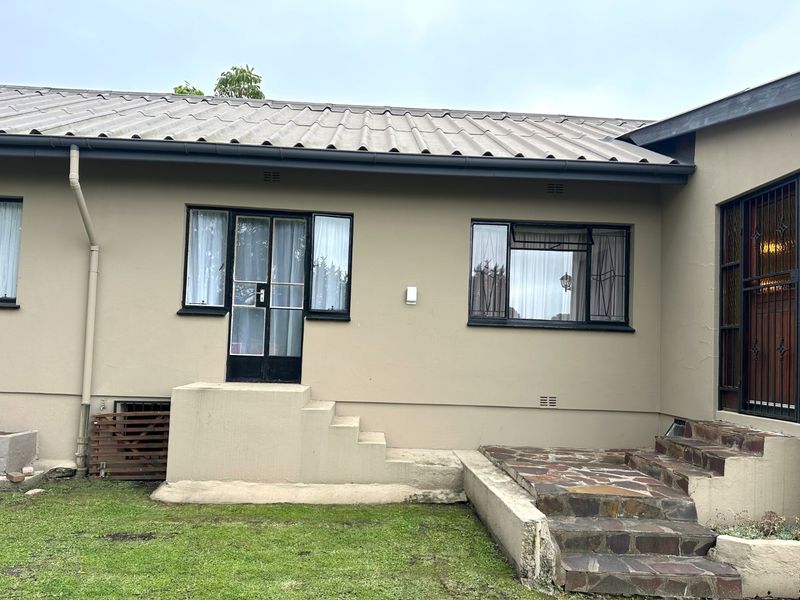 Rear exterior view of the house featuring a metal roof, concrete and stone-clad steps, and security-fitted windows and doors.