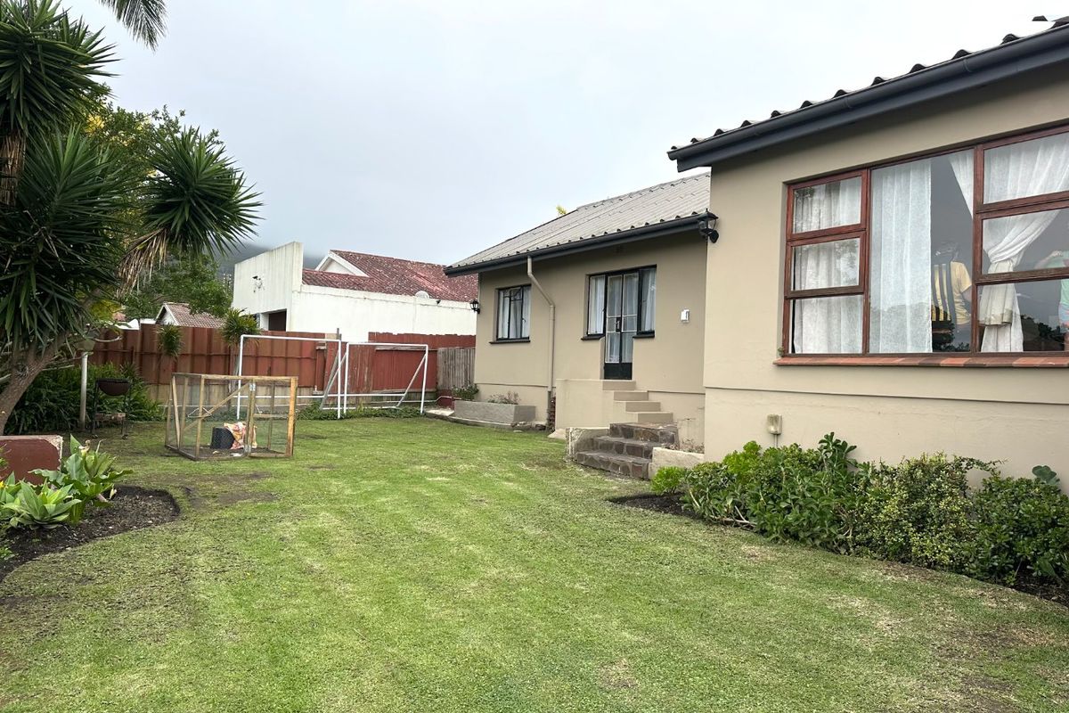 Rear view of the property featuring a lawned garden, timber-framed windows, and concrete steps leading to the rear entrance.