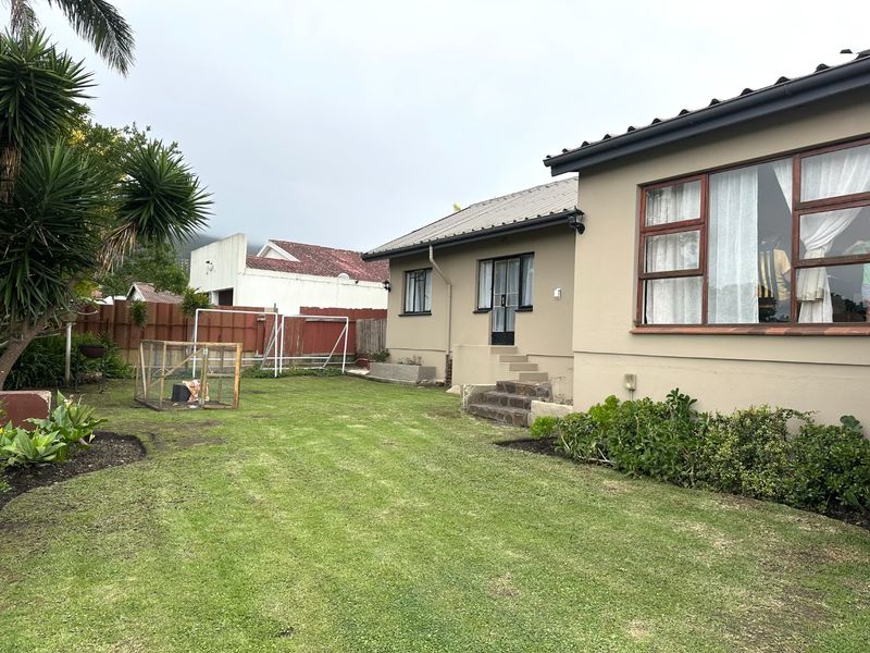 Rear view of the property featuring a lawned garden, timber-framed windows, and concrete steps leading to the rear entrance.