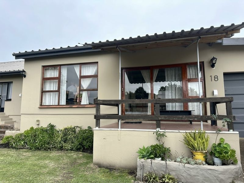 Front elevation of a single-story house featuring a raised patio, timber-framed windows, sliding glass doors, and a corrugated metal roof.