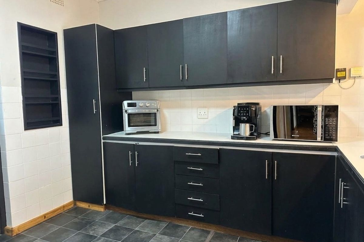 A functional kitchen featuring dark cabinetry, tiled backsplash, and dark floor tiles, providing ample storage and workspace.