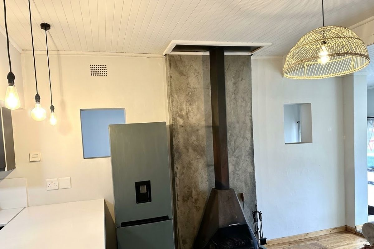 Living area featuring a unique concrete chimney breast with a freestanding fireplace, beadboard ceiling, and hardwood flooring, complemented by recessed wall niches.