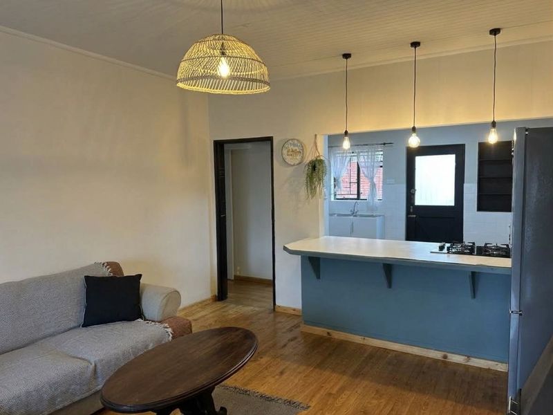Open plan living area featuring timber flooring, a breakfast bar with integrated hob, and a beadboard ceiling, connecting to the kitchen space.