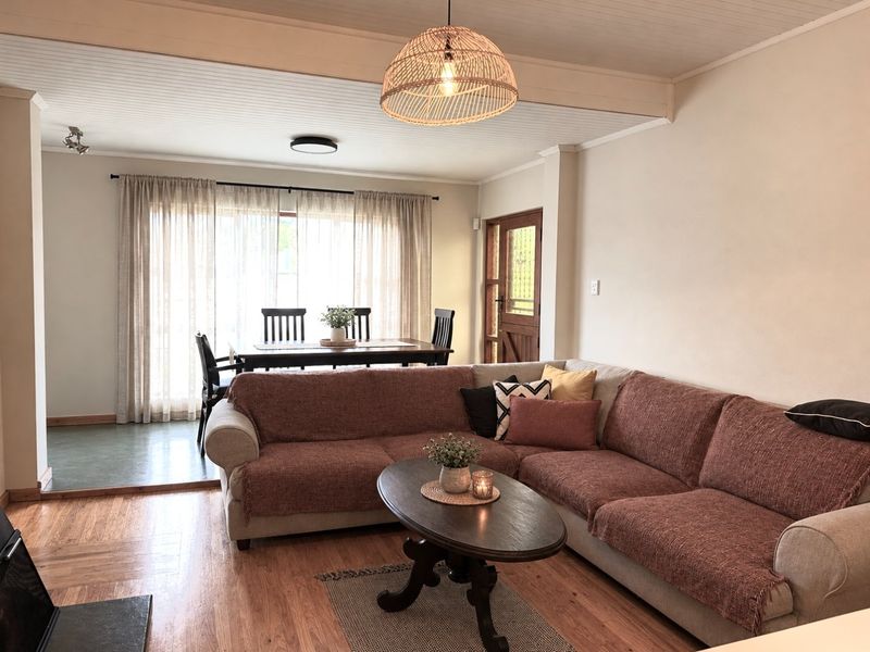 Spacious open-plan living and dining area featuring warm hardwood flooring, a timber-paneled ceiling, and natural light through large windows.