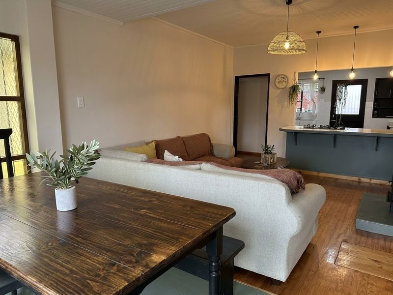 Open plan living and kitchen area featuring hardwood flooring, a central kitchen island with built-in cooktop, and warm pendant lighting throughout the space.
