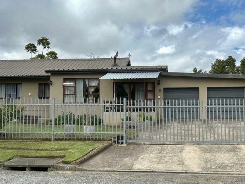 Front elevation of a single-story house featuring a double garage, concrete driveway, and secure metal perimeter fencing.