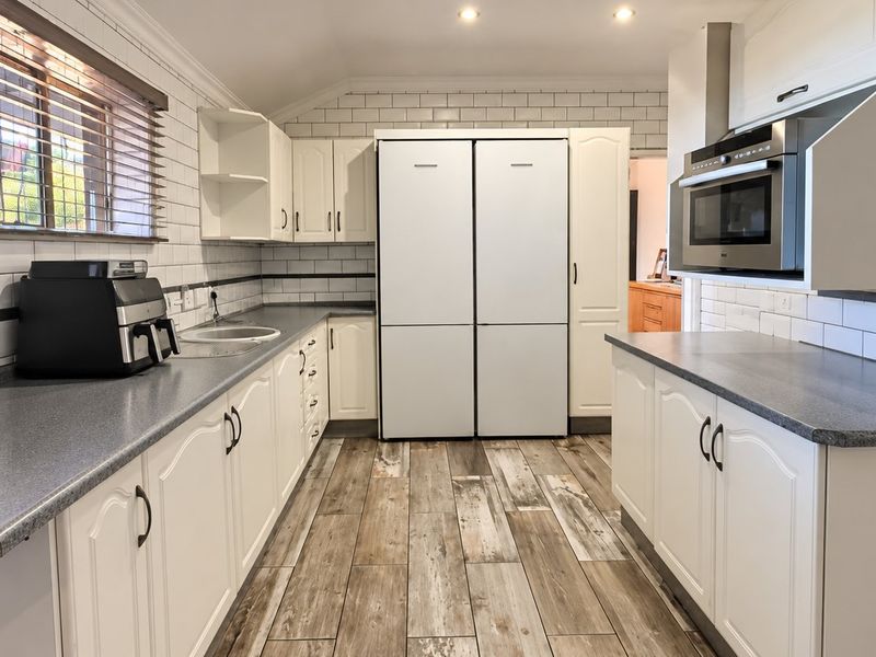 A well-maintained kitchen featuring white cabinetry, subway tile backsplash, grey laminate countertops, and wood-look tile flooring with integrated appliances.