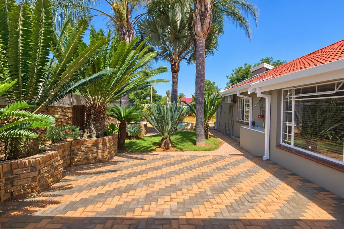 A well-maintained rear exterior featuring a patterned paved patio, brick retaining walls, and established garden landscaping alongside the house.