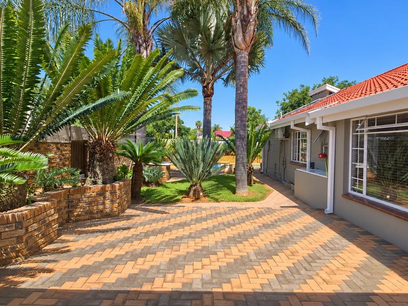 A well-maintained rear exterior featuring a patterned paved patio, brick retaining walls, and established garden landscaping alongside the house.