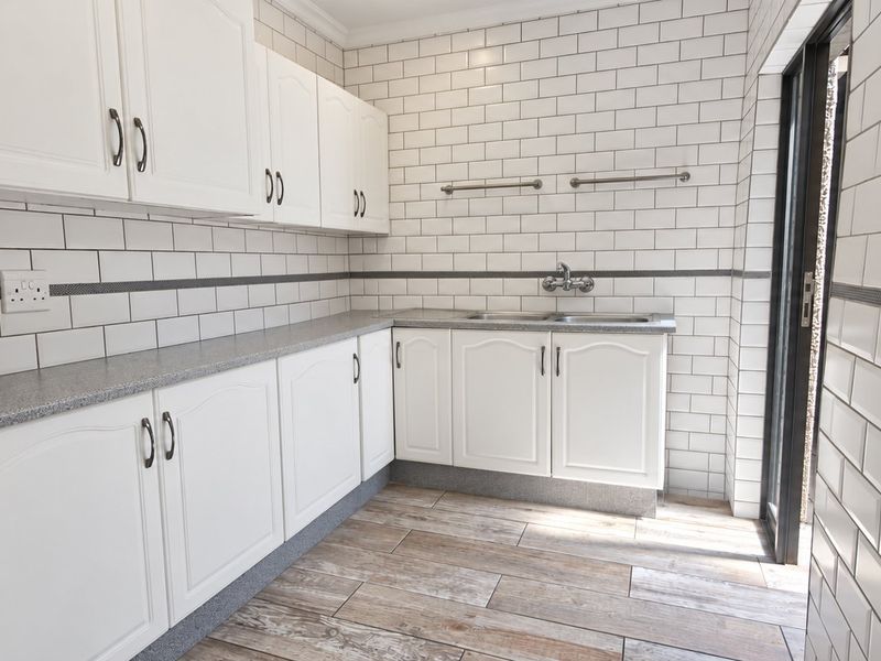 A clean and functional scullery featuring white cabinetry, subway tile walls, durable laminate countertops, and a double basin sink with wood-look tile flooring.