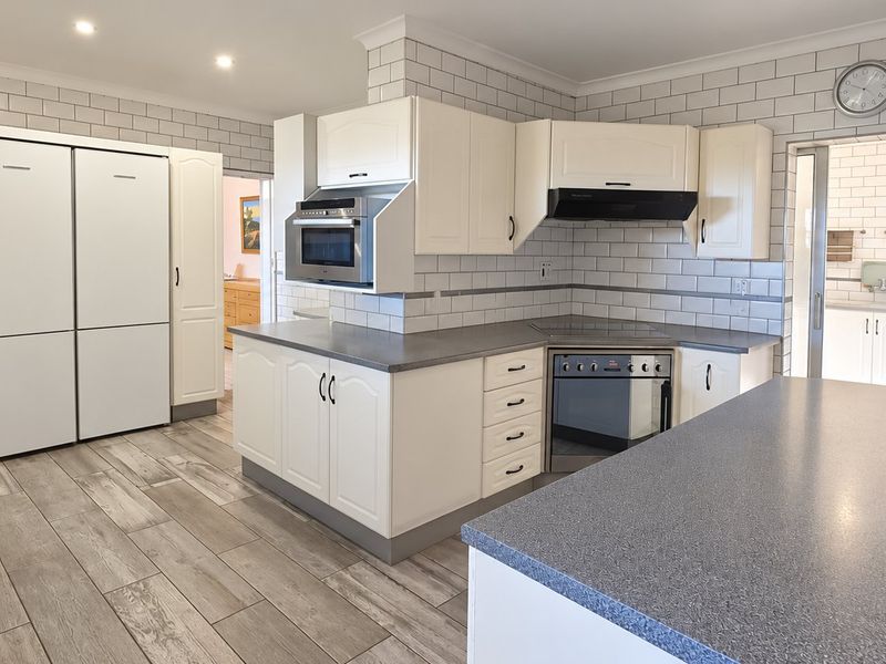 A well-maintained kitchen featuring white cabinetry, subway tile backsplash, stone-look laminate countertops, and integrated appliances with a functional layout.