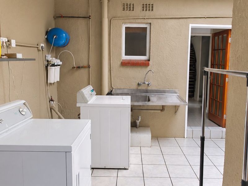 A functional outdoor laundry area featuring tiled flooring, a stainless steel sink, and a corrugated metal roof structure.
