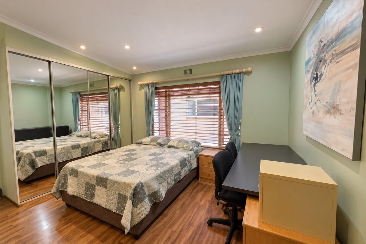 A well-maintained bedroom featuring timber-look flooring, recessed downlights, and a large mirrored built-in wardrobe, offering a clean and functional living space.