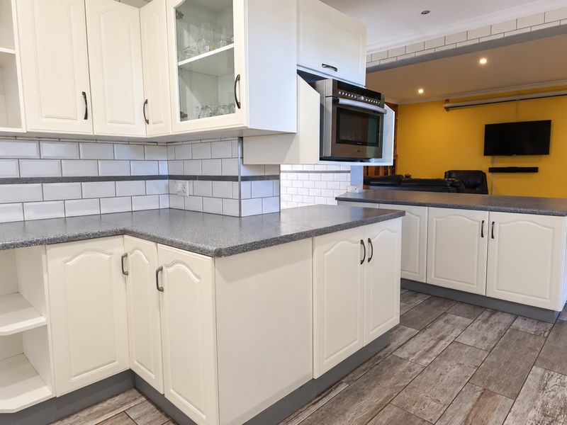 Open plan kitchen featuring white cabinetry, subway tile backsplash, and laminate countertops, seamlessly flowing into the adjacent living area with tiled flooring.