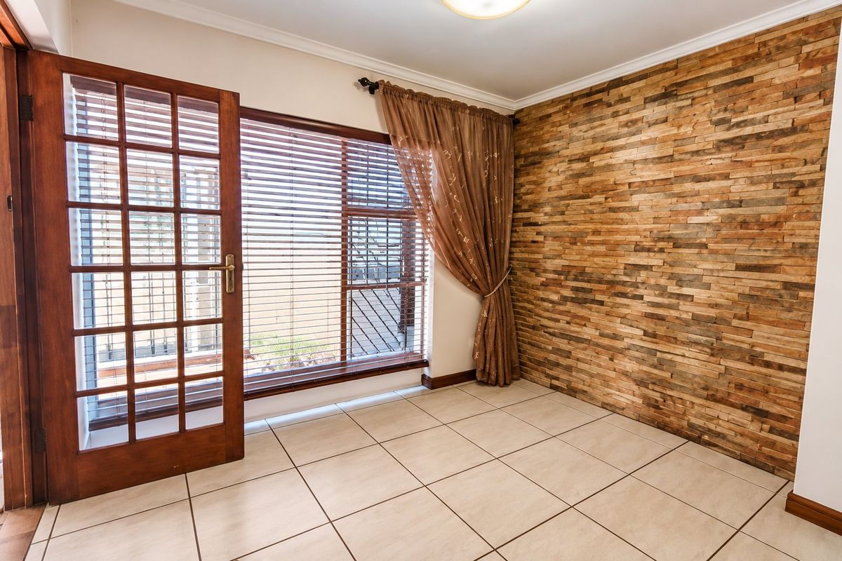 A bright living area featuring a textured stone veneer accent wall, neutral ceramic floor tiles, and a timber-framed glass door leading to the exterior.
