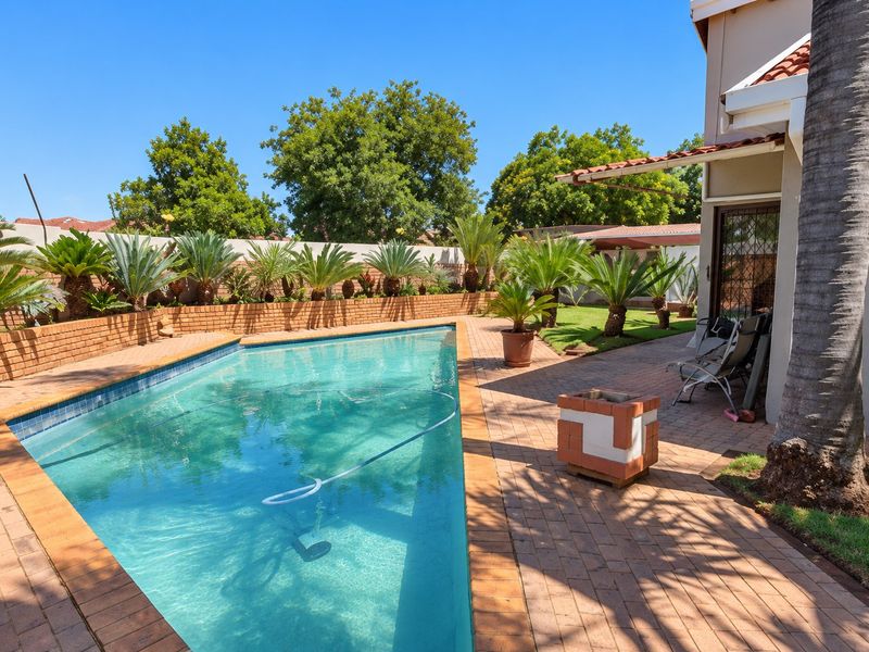 A well-maintained outdoor pool area featuring brick paving, a retaining wall, and established landscaping, providing a pleasant space for outdoor relaxation.