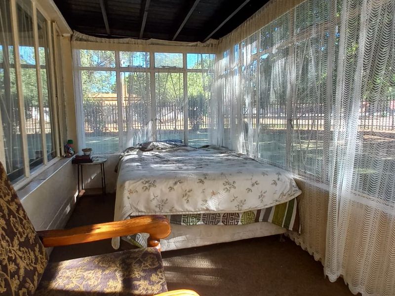 An enclosed patio area featuring large glass windows, exposed timber ceiling beams, and carpeted flooring, offering a bright space with views of the garden.