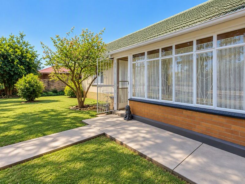 A well-maintained rear exterior view featuring a concrete pathway, brick facade, and large windows overlooking a landscaped garden.