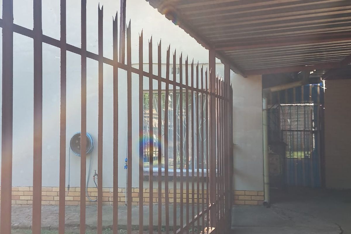 Rear exterior view showing a paved area with a corrugated metal roof structure and metal security fencing along the perimeter.