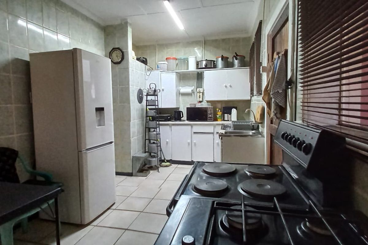 A functional kitchen featuring tiled walls, built-in cabinetry, a stainless steel sink, and an electric stove, offering a dated aesthetic ready for modernization.