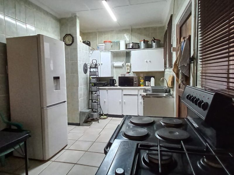 A functional kitchen featuring tiled walls, built-in cabinetry, a stainless steel sink, and an electric stove, offering a dated aesthetic ready for modernization.