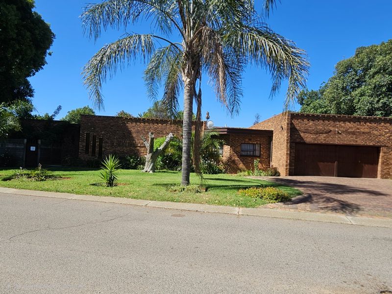 A single-story face brick house featuring a paved driveway, double garage, and a well-maintained front garden with mature palm trees.