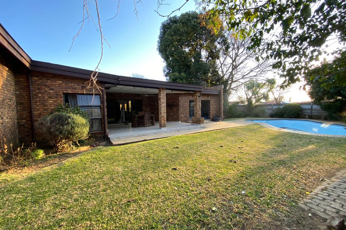 Rear view of the property featuring a brick facade, a covered patio area, and a swimming pool set within a garden.