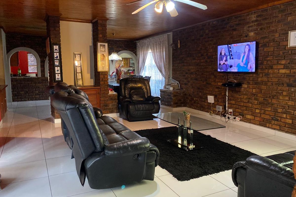 Spacious living room featuring exposed brick walls, a warm timber ceiling, and tiled flooring, creating a cozy and traditional atmosphere.