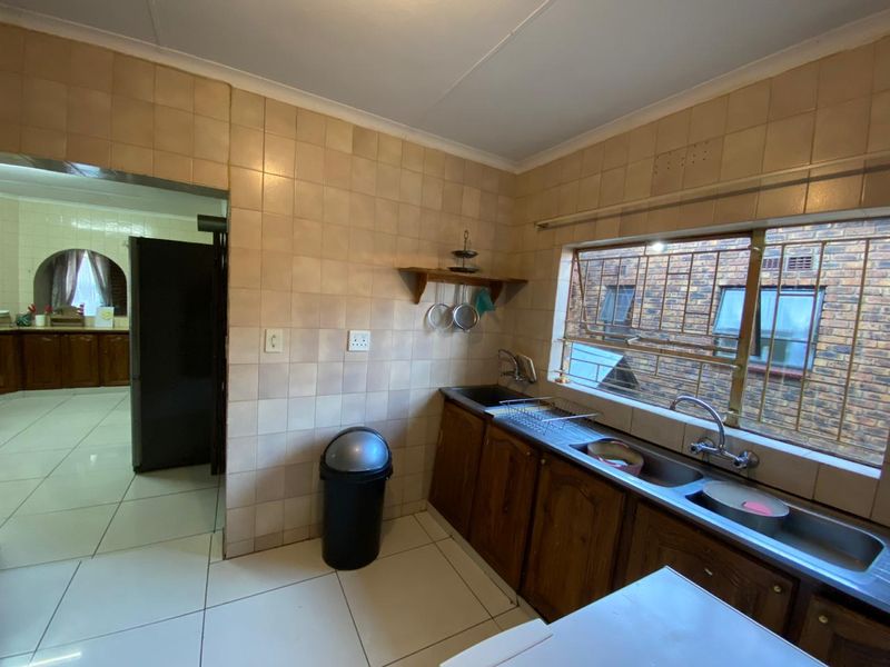 A functional kitchen featuring wooden cabinetry, a double sink with mixer tap, and tiled splashbacks, with a view through a window with security bars.