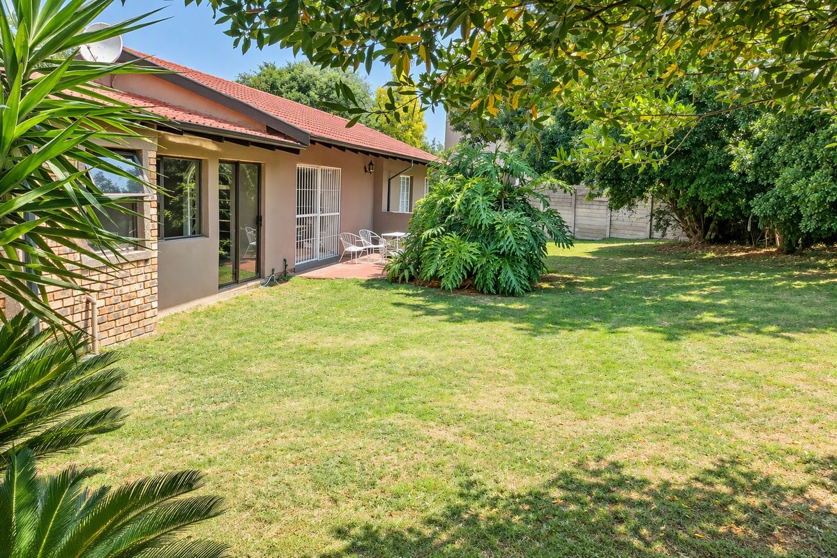 Rear view of the house featuring a tiled roof, brick and plaster facade, sliding glass doors with security gates, and a paved patio area.