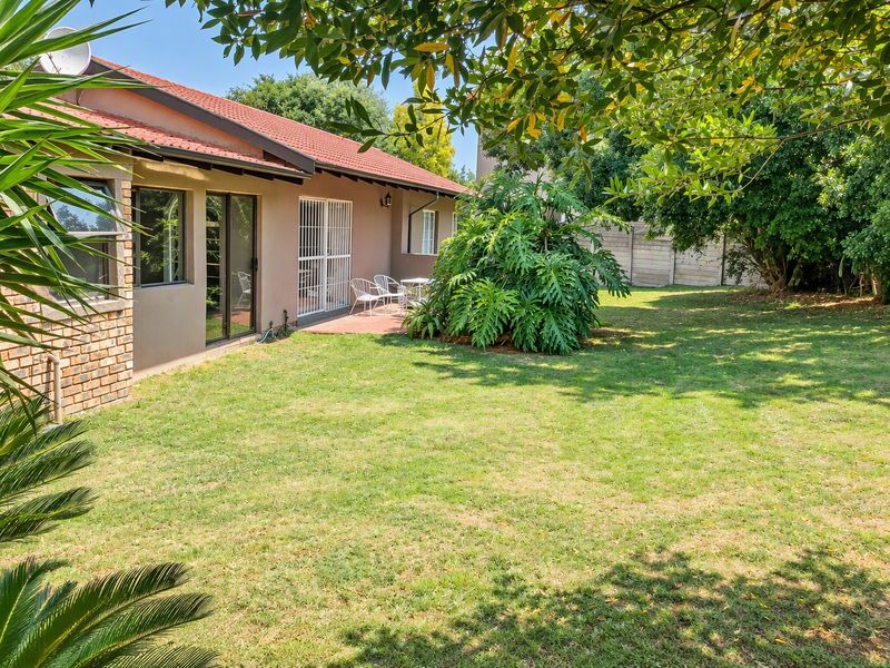 Rear view of the house featuring a tiled roof, brick and plaster facade, sliding glass doors with security gates, and a paved patio area.