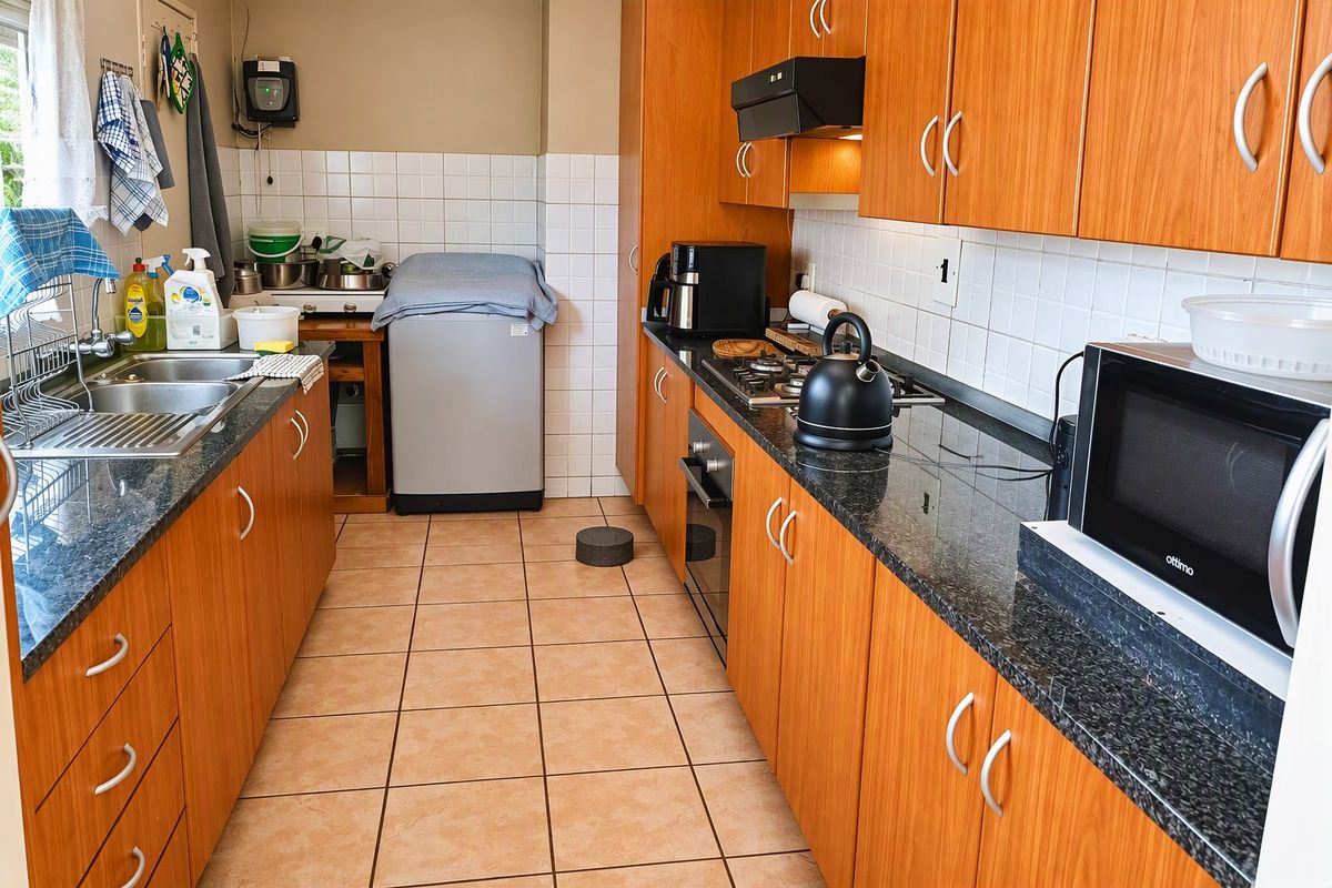 Functional galley-style kitchen featuring wood-look cabinetry, granite countertops, built-in oven, gas hob, and tiled flooring with a dedicated laundry area.