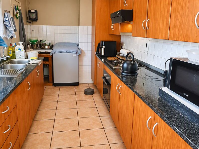 Functional galley-style kitchen featuring wood-look cabinetry, granite countertops, built-in oven, gas hob, and tiled flooring with a dedicated laundry area.